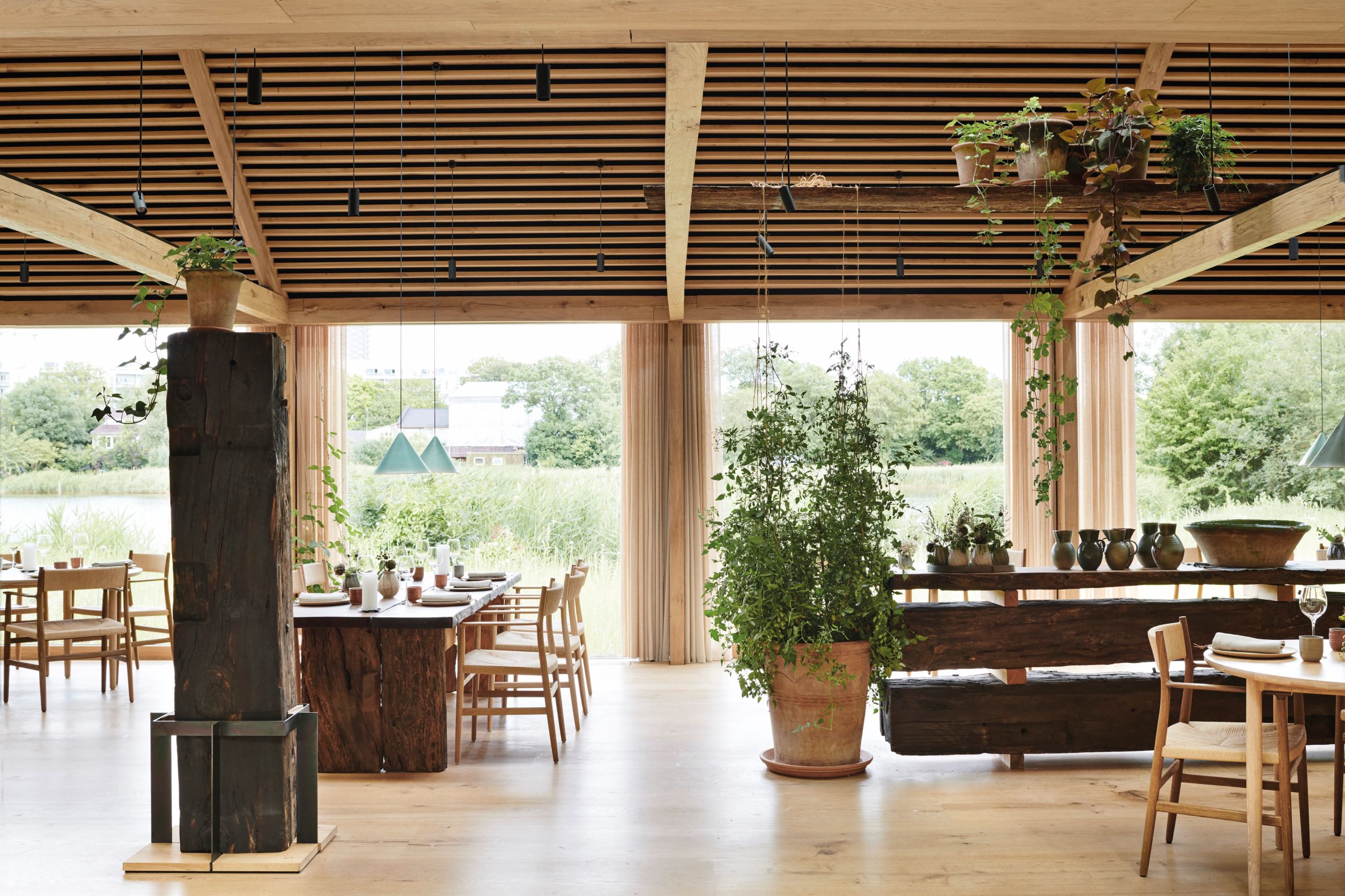 由 Studio David Thulstrup 所設計的餐廳用餐空間，以原木和大量植栽營造出自然愜意的空間氛圍。