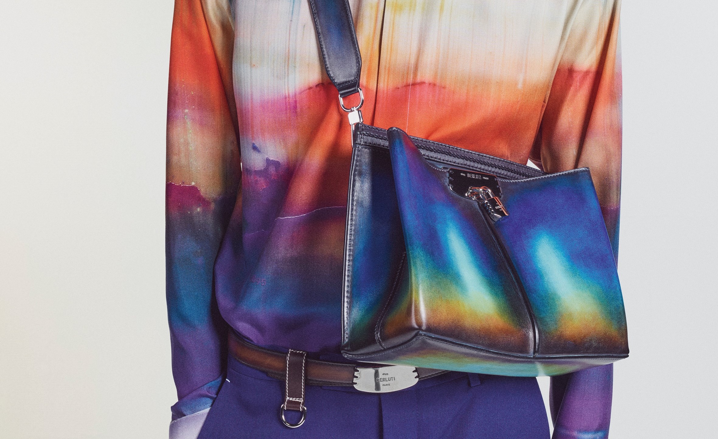 率性俐落的皮革斜背包，上頭的皮革同樣以 Lev Khesin 的色彩變化風格為設計，與身穿的襯衫創造了一致性，也為正式的包款添加活潑感。