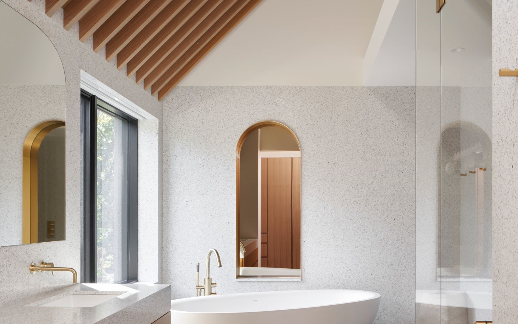 挑高的主臥衛浴，以木質格柵包覆斜天花板，消弭斜屋頂的銳利尖角，落地開窗引進自然光與綠意，備感舒適。